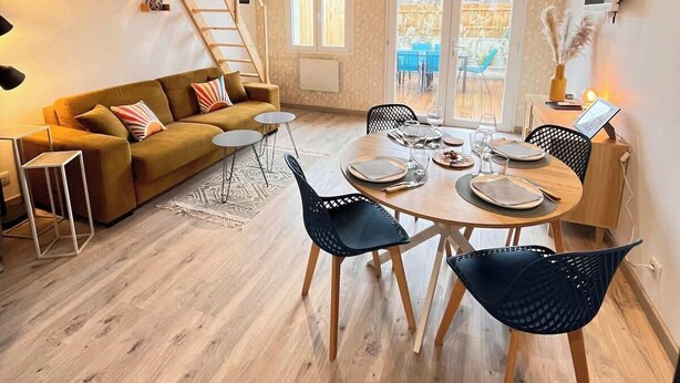 A cozy living room with a sofa, a dining table with chairs, a ladder, and a TV mounted on the wall. - 2/ Pavillon neuf proche plage (Saint-Jean-de-Monts)