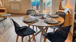 A dining area with a round table set for four, surrounded by black chairs with wooden legs. - 2/ Pavillon neuf proche plage (Saint-Jean-de-Monts)