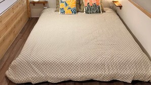 A bedroom with a sloped ceiling, a wooden bed frame, a patterned bedspread, two pillows, and a nightstand with a lamp. - 2/ Pavillon neuf proche plage (Saint-Jean-de-Monts)