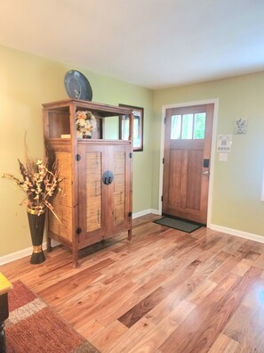 A wooden cabinet with a clock, a door, and a doormat in a room with wooden flooring and light green walls. - Palm Paradise 5 min to Downtown 5 min to the Beaches (St. Augustine)