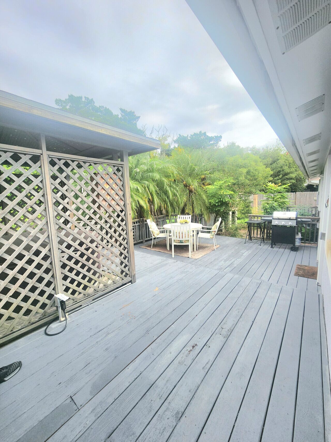 A wooden deck with a covered seating area, a grill, and a lattice fence.