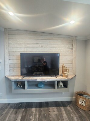 A flat-screen TV mounted on a wooden wall with a built-in shelf below. - Coral Cove Cottage-Walk to Beach-Near Downtown (St. Augustine)