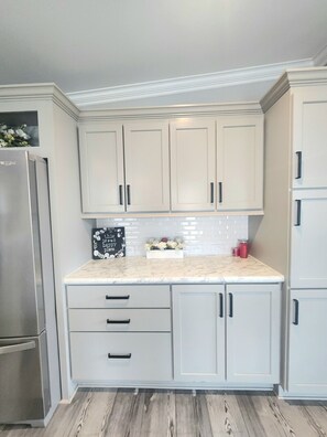 A kitchen with white cabinets, a marble countertop, and a stainless steel refrigerator. - Coral Cove Cottage-Walk to Beach-Near Downtown (St. Augustine)