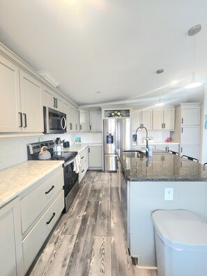 A spacious kitchen with white cabinetry, a central island, stainless steel appliances, and a wooden floor. - Coral Cove Cottage-Walk to Beach-Near Downtown (St. Augustine)