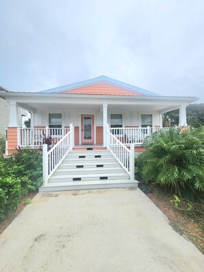 A two-story house with a front porch, a red door, and a staircase leading to the entrance. - Coral Cove Cottage-Walk to Beach-Near Downtown (St. Augustine)
