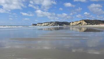 A beach with a clear sky, calm water, and rocky cliffs in the background.