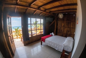 A room with a bed, a fan, a TV, and a view of the beach.