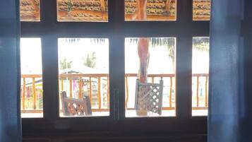 A room with a view of a wooden deck and a thatched roof structure outside.