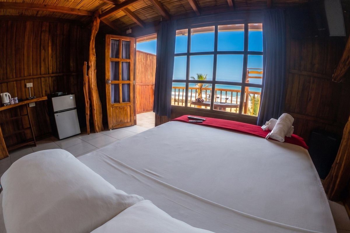 A room with a bed, a small kitchenette, and a large window with a view of the beach.
