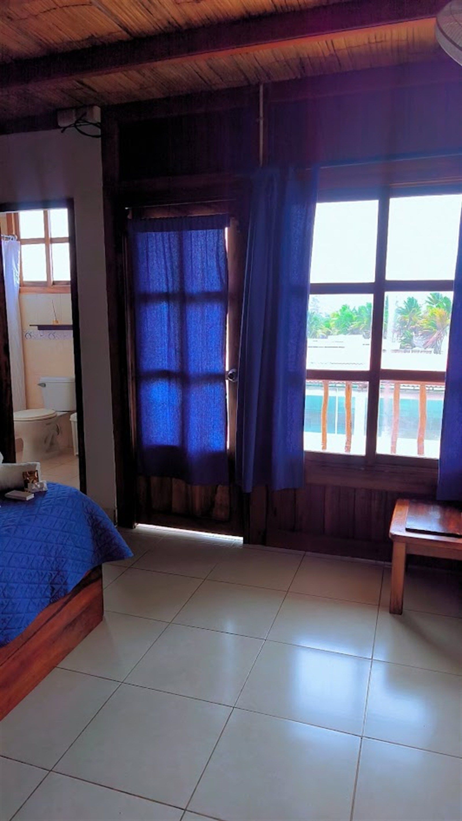 Una habitación con cama, una mesita y una ventana con cortinas.