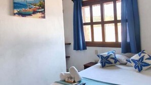Ein Schlafzimmer mit Holzbalkendecke, einem Bett mit blauer Bettwäsche, einem Fenster mit blauen Vorhängen und einem Gemälde an der Wand.