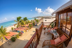A beachfront property with a balcony overlooking the ocean, a patio with seating, and a view of the beach and ocean.