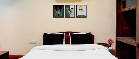 A hotel room with a bed, an air conditioner, and three framed artworks on the wall.