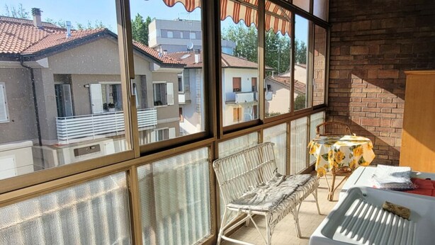 Ein Balkon mit einem weißen Metallstuhl, einem kleinen Tisch mit gelber Tischdecke und einer weißen Heizung.
