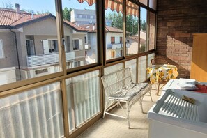 Een balkon met een witte metalen stoel, een tafeltje met een gele tafelkleed en een witte radiator.