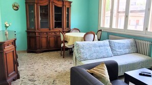 Ein Zimmer mit Steinboden, einem Holzschrank, einer Couch, einem Tisch und einem Fenster mit Blick auf Gebäude.