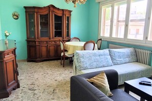 Ein Zimmer mit Steinboden, einem Holzschrank, einer Couch, einem Tisch und einem Fenster mit Blick auf Gebäude.