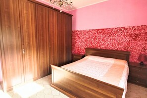 Een slaapkamer met een houten bed, een kledingkast en een roze muur met een bloemenmotief.