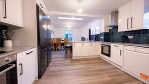 Une cuisine moderne avec des meubles blancs, un réfrigérateur en acier inoxydable, un lave-vaisselle et une table à manger en bois avec des chaises.