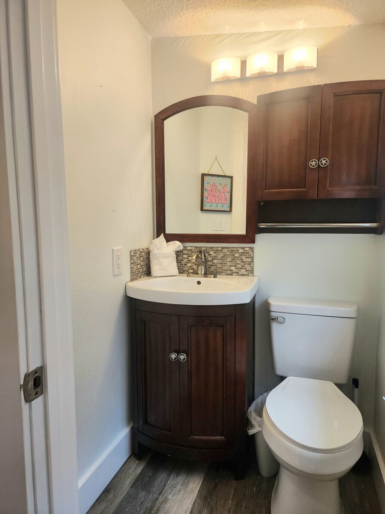 Een badkamer met een witte wasbak, een spiegel, een toilet en houten kastjes.