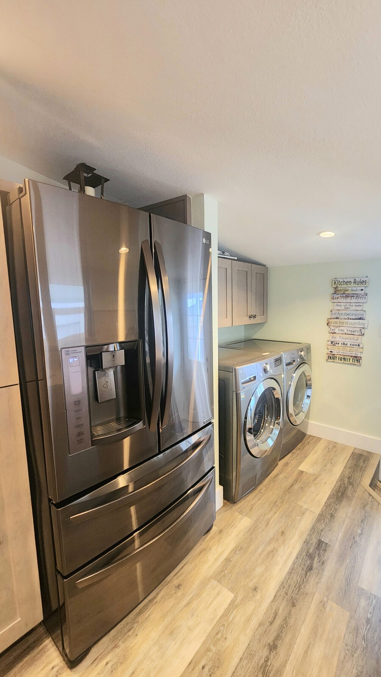 A kitchen with stainless steel appliances, a washing machine, and a wall with kitchen rules.