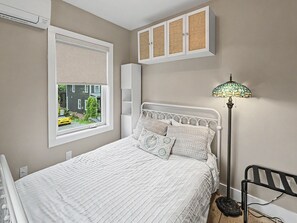Een slaapkamer met een bed, een raam met uitzicht op een gebouw, een lamp en een kast.