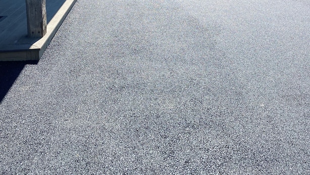Ein überdachter Parkbereich mit Holzzaun, einem Schotterweg und einem geparkten Auto.
