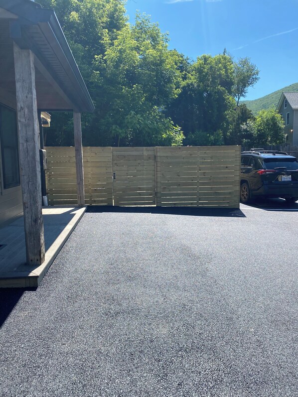 A covered parking area with a wooden fence, a gravel driveway, and a parked car. - Private Terrace + Mt Beacon Views + Near Roundhouse (Beacon)