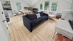 Ein modernes Loft mit hohen Decken, einem dunkelblauen Sofa, einem Esstisch, einer Küchenzeile und großen Fenstern.
