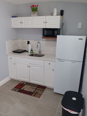A kitchen with white cabinets, a stainless steel sink, a microwave, a white refrigerator, and a trash bin. - Villa Paris apartment#2 close to airport, hospital, stadium, market, store (Tampa)