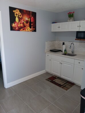 A kitchen with white cabinets, a tiled backsplash, a sink, and a painting on the wall. - Villa Paris apartment#2 close to airport, hospital, stadium, market, store (Tampa)