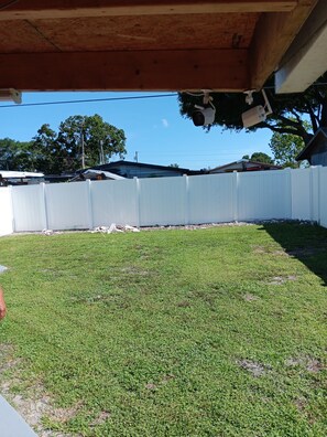A grassy yard with a white fence, a wooden deck, and a building in the background. - Villa Paris apartment#2 close to airport, hospital, stadium, market, store (Tampa)