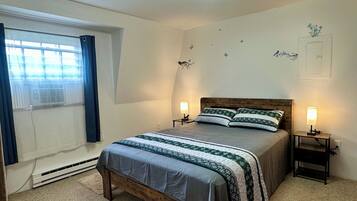 Un dormitorio con una cama, dos mesitas de noche, una ventana con cortinas y adornos en la pared.