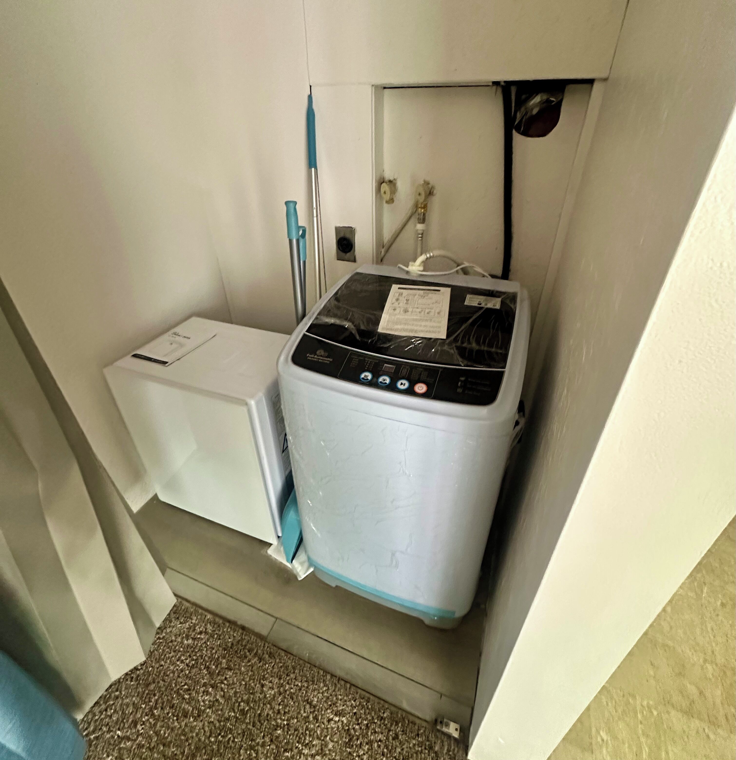 A compact, white, wall-mounted washer and dryer unit with a control panel and a small instruction manual.