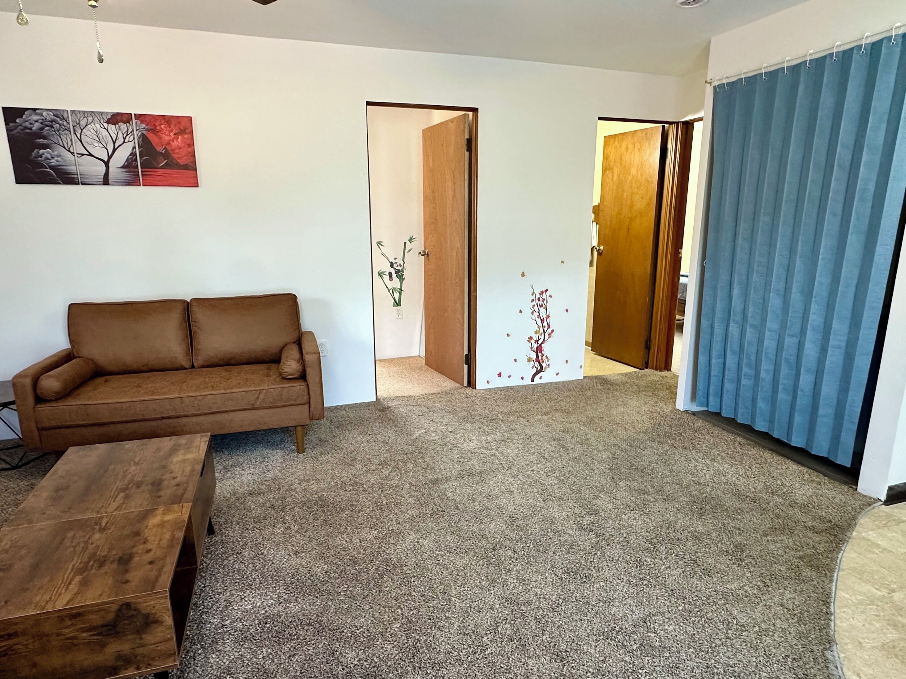 Una sala de estar con un sofá marrón, una mesa de centro de madera y piso alfombrado.