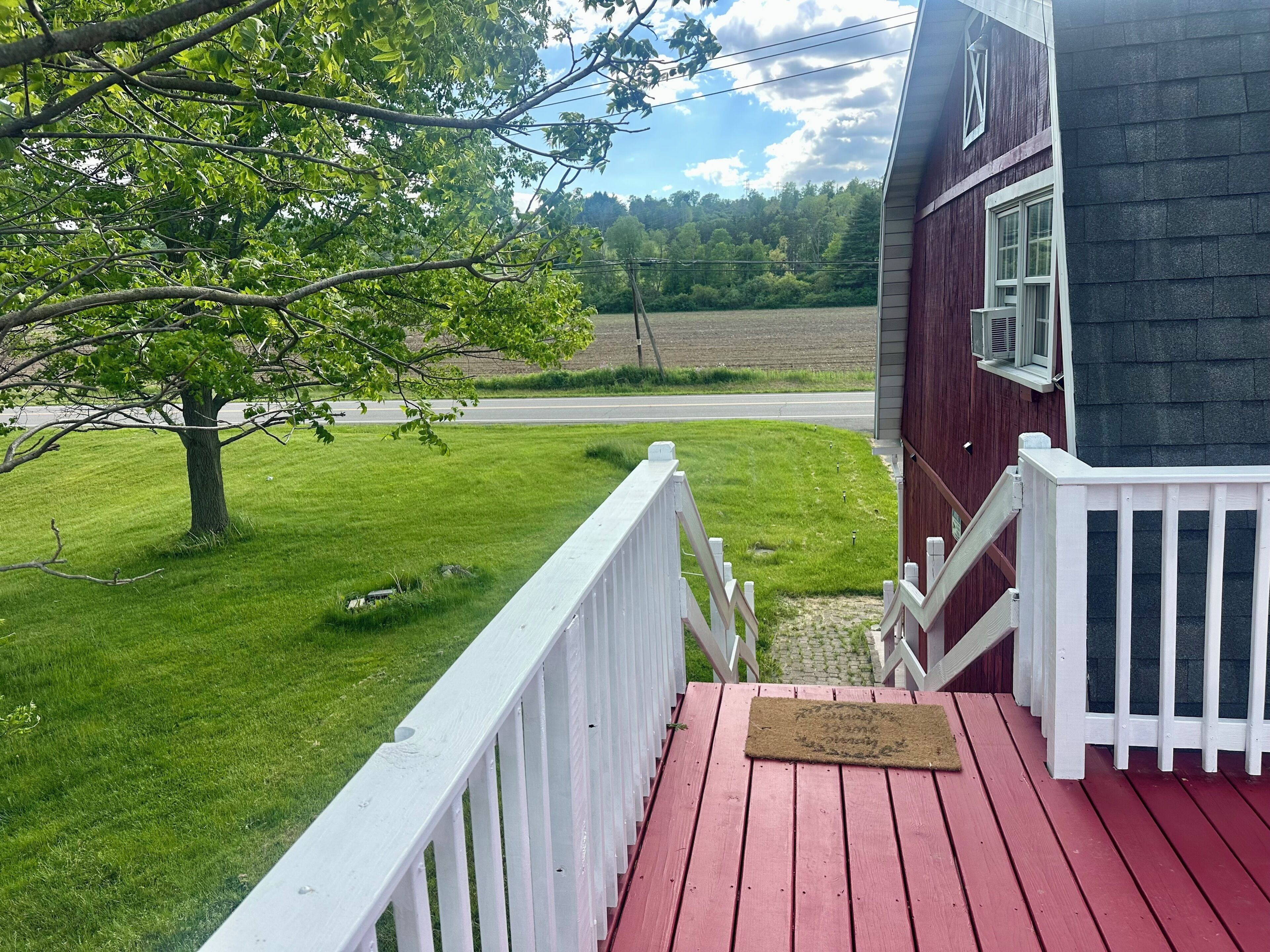 Une terrasse en bois avec une balustrade blanche, une porte rouge et une boîte aux lettres.