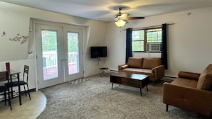 A living room with a ceiling fan, a sofa, a coffee table, a TV, and a dining area with chairs and a table. - Rustic Barn Apartment with Mountain and Farm Views, 2-bedroom, 1-bath apartment (Apalachin)