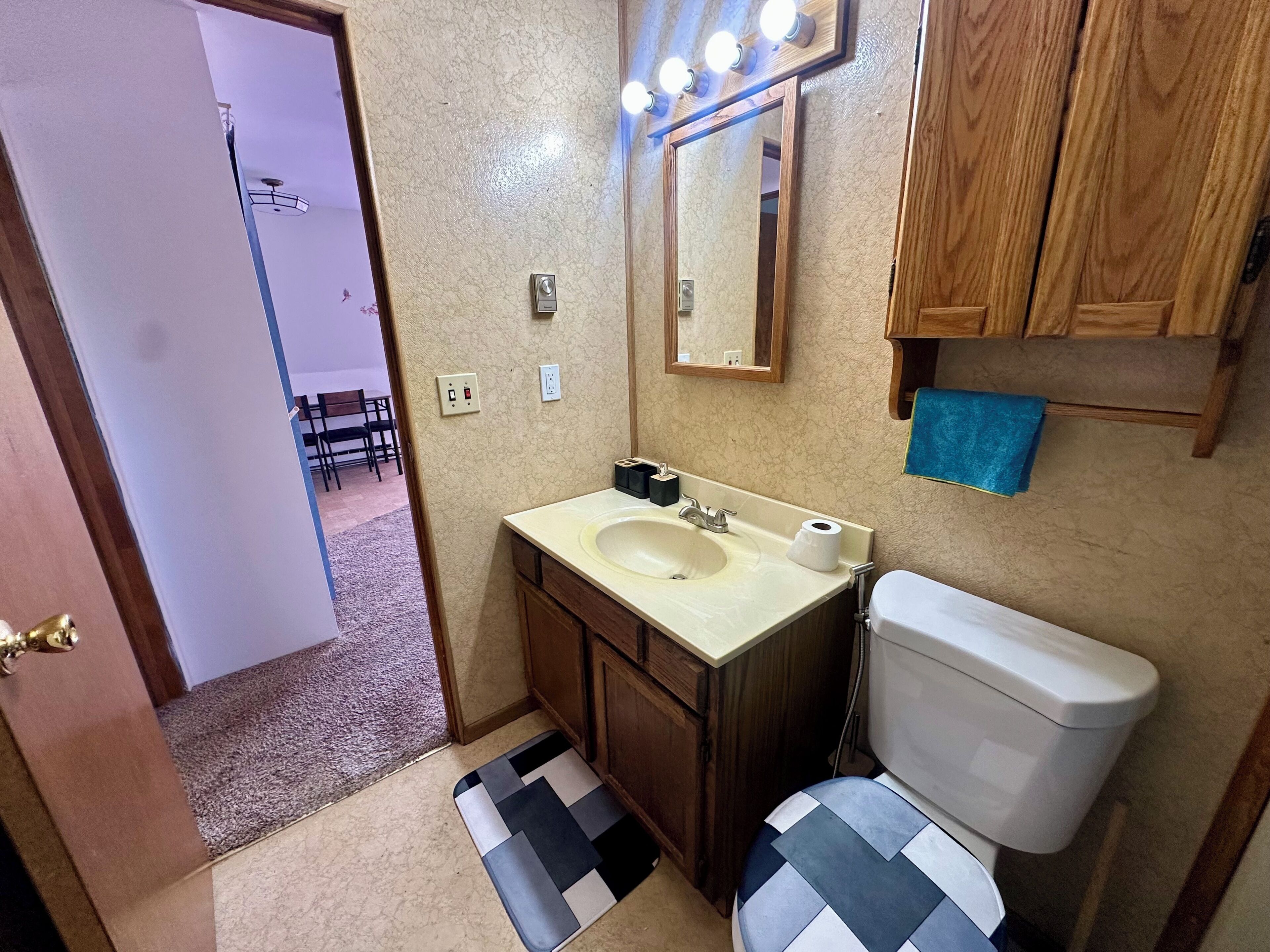 Une salle de bain avec un lavabo, un miroir et des toilettes. Il y a un tapis sur le sol et une serviette accrochée au mur.