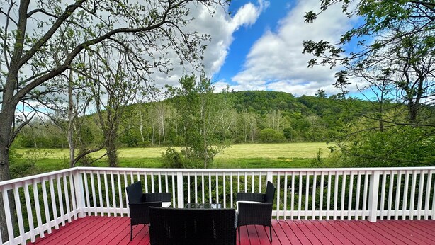A red deck with white railings, two black wicker chairs, and a glass table. - Rustic Barn Apartment with Mountain and Farm Views, 2-bedroom, 1-bath apartment (Apalachin)