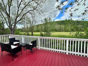 A red deck with white railings, black wicker furniture, and a view of a green landscape. - Serene Mountain & Farm Retreat with Deer Views in Apalachin 2 bedrooms apt (Apalachin)