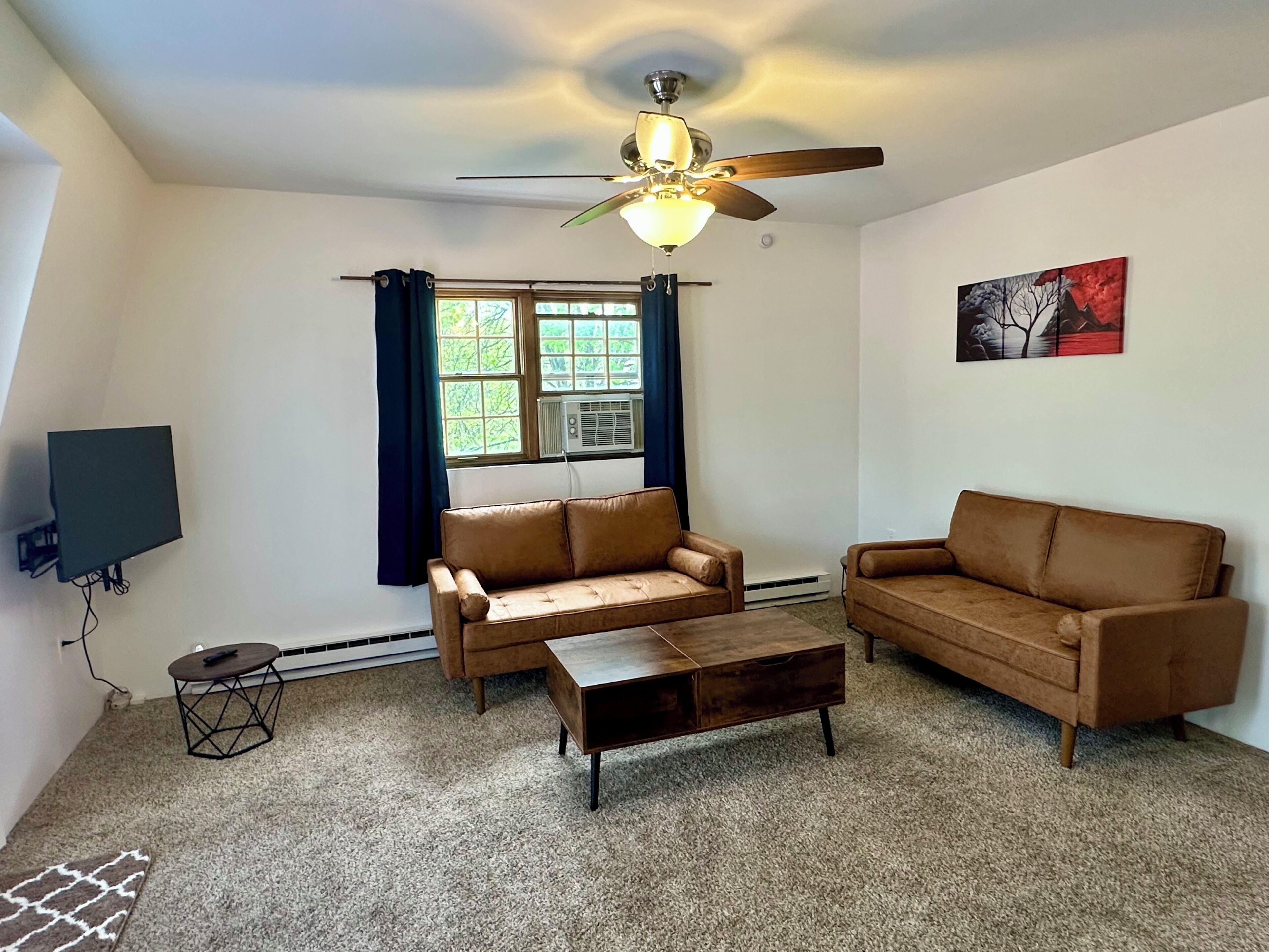 A living room with a ceiling fan, two sofas, a coffee table, a TV, and a window with curtains.
