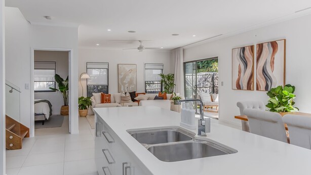 Una cocina moderna con una isla central, un comedor con mesa blanca y una sala de estar con sof á y un ventanal grande.
