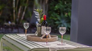 A table with a bottle of wine, two glasses, and a woven basket. - Sunrays Sanctuary – 350m to Beach & Pet-Friendly (Casuarina)