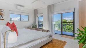 A bedroom with a bed, a nightstand, a lamp, a window, and a balcony with a view. - Sunrays Sanctuary – 350m to Beach & Pet-Friendly (Casuarina)