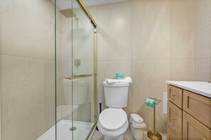 Ein modernes Badezimmer mit einer gläsernen Duschkabine, einer weißen Toilette und einem goldenen Waschtisch mit weißer Arbeitsplatte.
