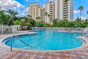 Ein Swimmingpool mit weißem Zaun, Palmen und einem Hotel im Hintergrund.