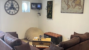 Un salon avec un canapé en cuir marron, une horloge murale, un téléviseur à écran plat et une œuvre d’art représentant une carte du monde.