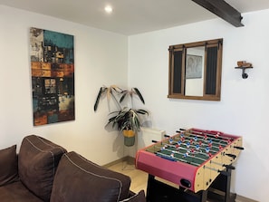 Um quarto com mesa de futebol, sofá, planta em vaso e um quadro na parede.