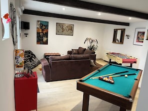 Uma sala de estar com mesa de bilhar, sofá, mesa de futebol de mesa e televisão.