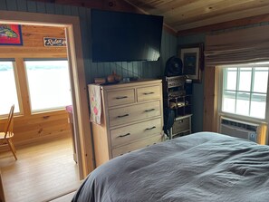 Ein Zimmer mit Holzboden, einem Bett, einem Schminktisch, einem Fernseher und einem Fenster.